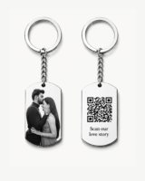 Hidden Message Photo Keychain: Two silver keychains displayed on a clean light background. One rectangular pendant features a black-and-white couple photo, and the other pendant shows a QR code with the words “Scan our love story.