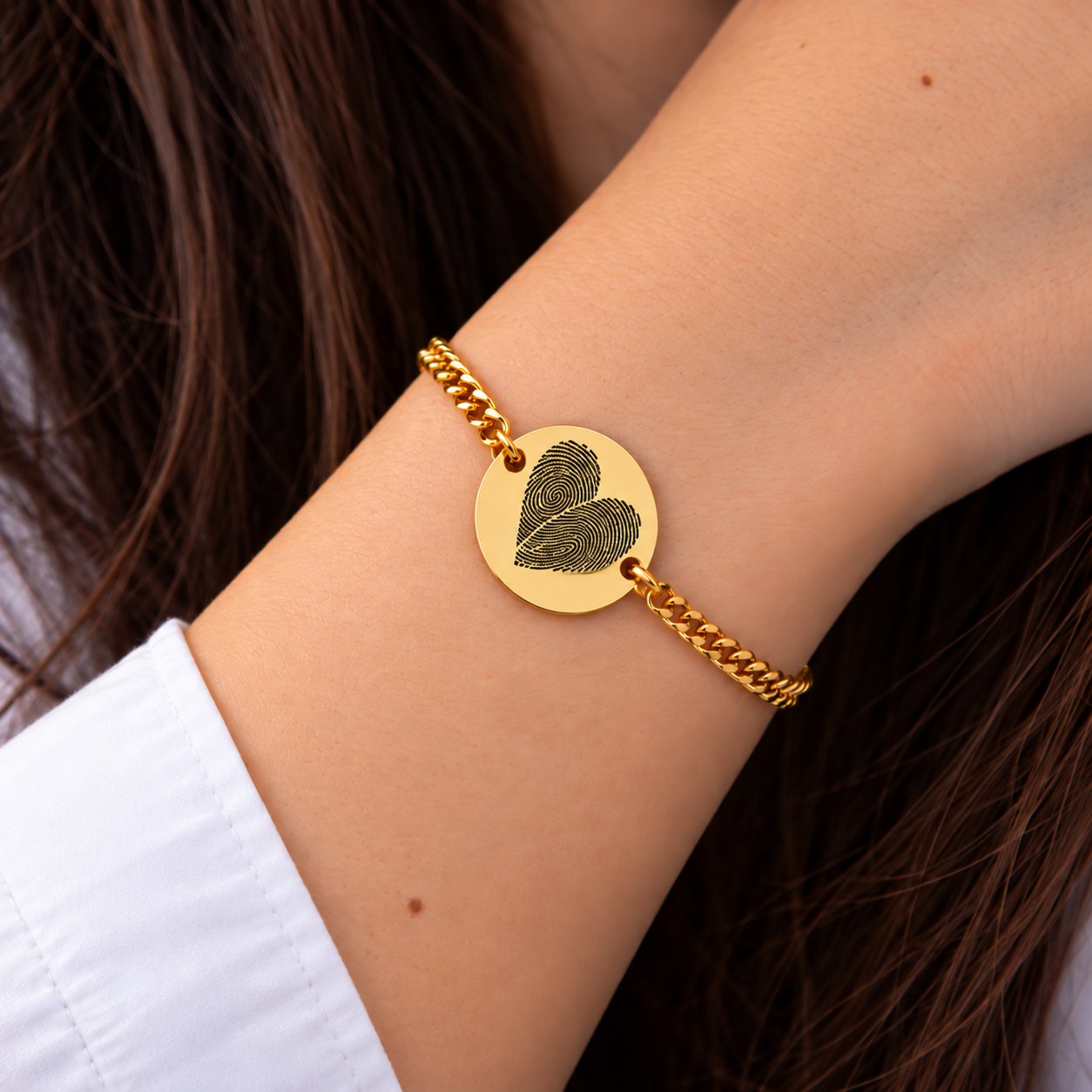 Woman wearing a gold two fingerprint heart bracelet with Cuban chain — two actual fingerprints engraved as one heart on a round disc. Personalized couples bracelet, everyday memorial keepsake jewelry.