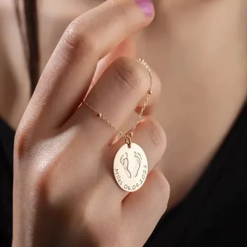 Custom baby footprint necklace, sentimental jewelry for moms, with a mother holding the engraved pendant in her hands.